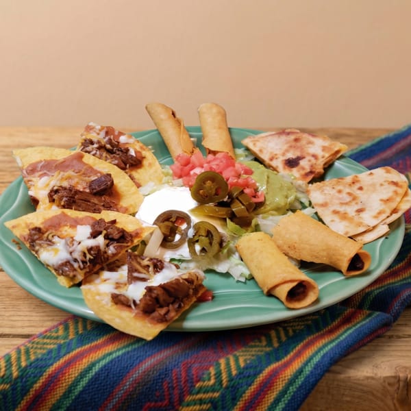 A platter of nachos, taquitos, and quesadillas with guacamole, sour cream, and jalapeños.